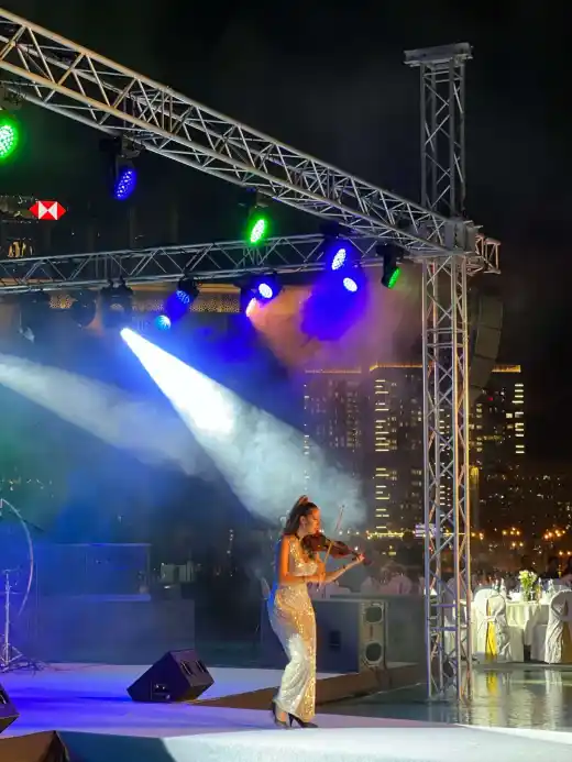 A violinist playing in a spotlight on an outdoor stage against a city skyline