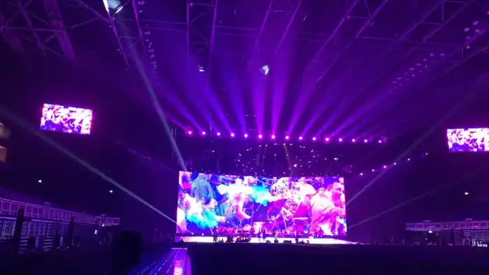 An arena stage with a full-width LED screen and purple beams cutting across an empty auditorium